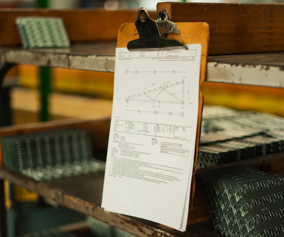 A clipboard holding a sheet of paper displaying a truss diagram, hanging from a metal shelf