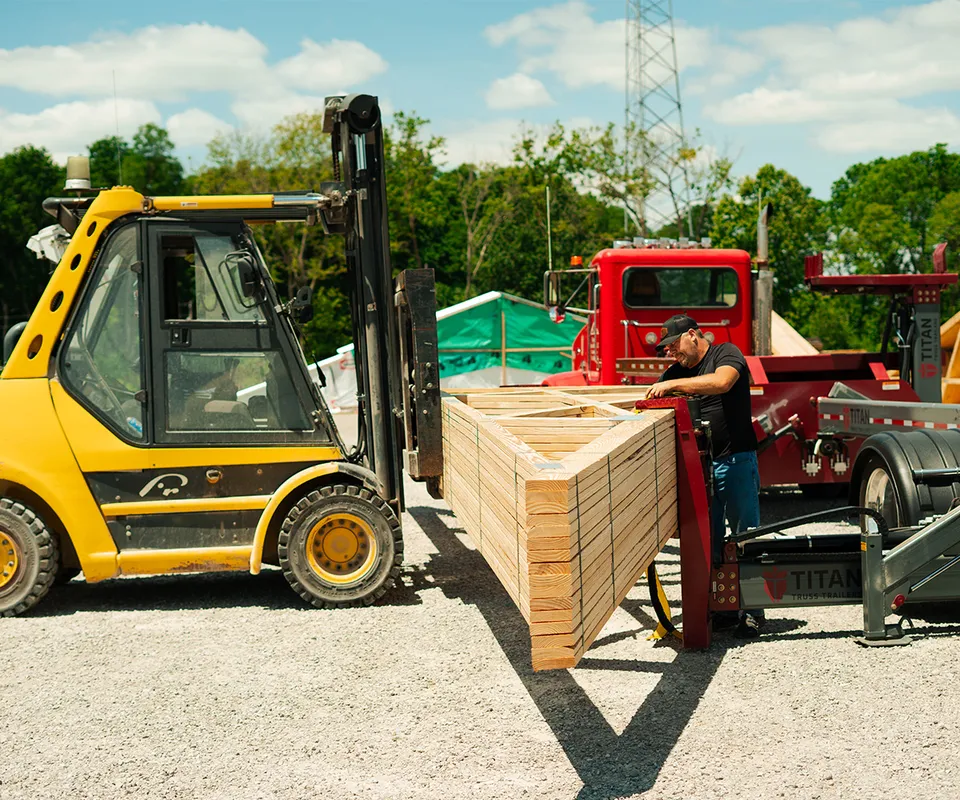 A yellow forklift is lifting a stack of trusses on to a truck for transportation